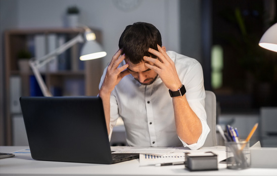 Frustrated freight agent holding his head in his hands while working late at his desk, symbolizing the growing red flags and stress in an unbalanced broker relationship before finding better support at D&L Transport.